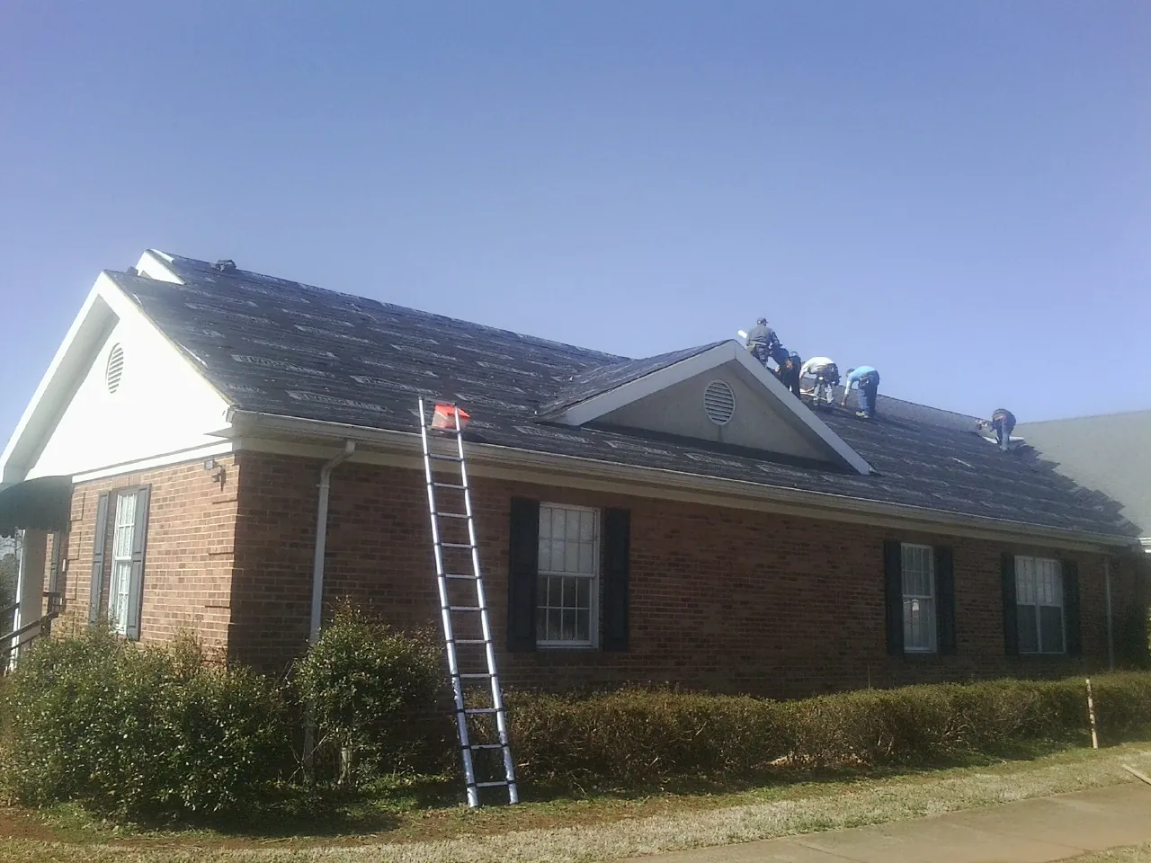 Crew tearing shingles off a brick ranch roof with a ladder set — Metal Roof Repair work by our crew in Hickman