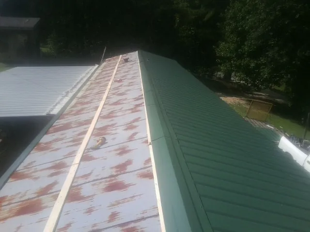 Old rusted panels beside newly installed green metal roofing — Wind Damage Roof Repair by Roofing Brothers in Hickman