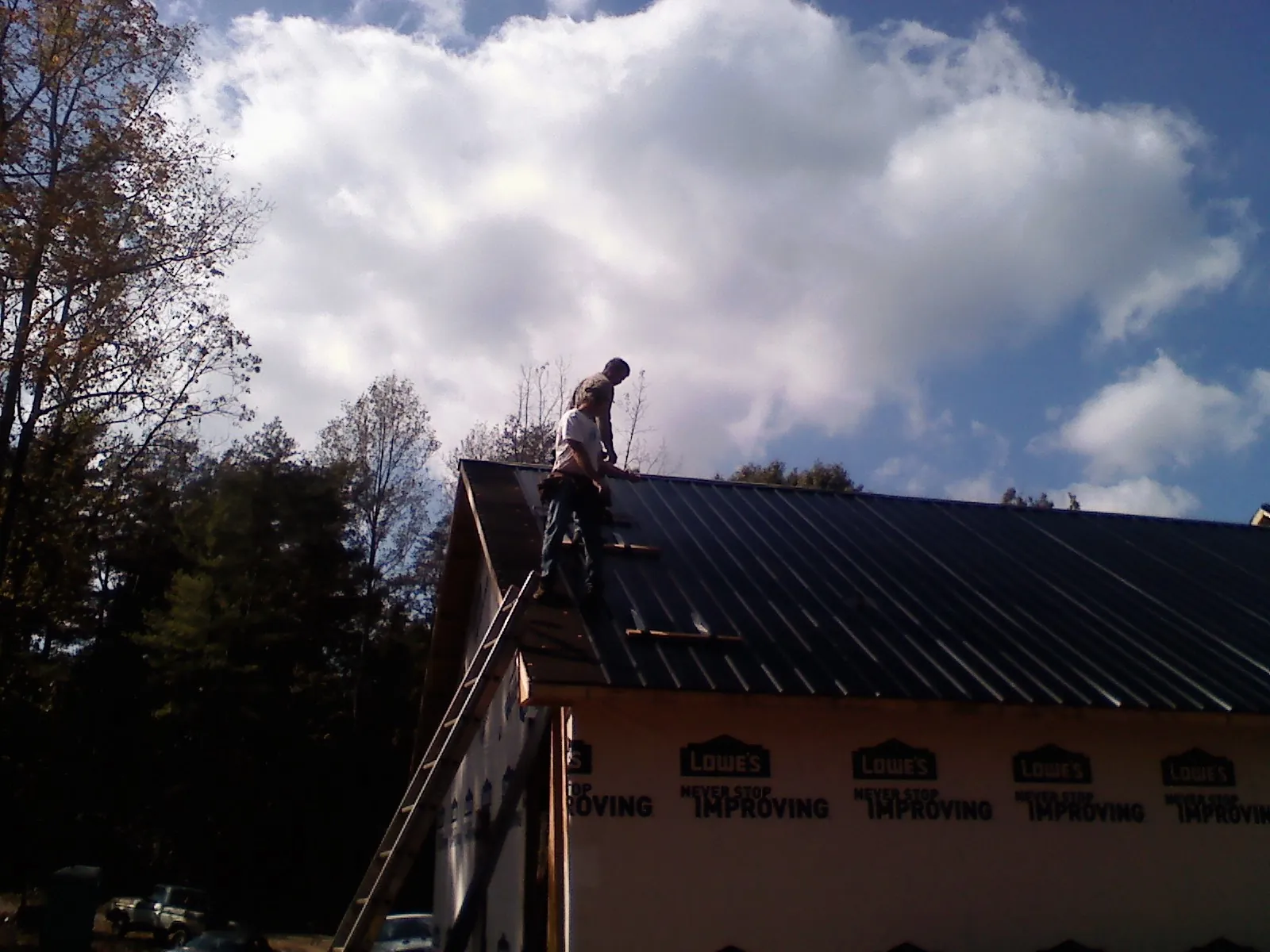 Roofer fastening dark metal panels high against a cloudy sky, from a Roof Inspection job in Hickman