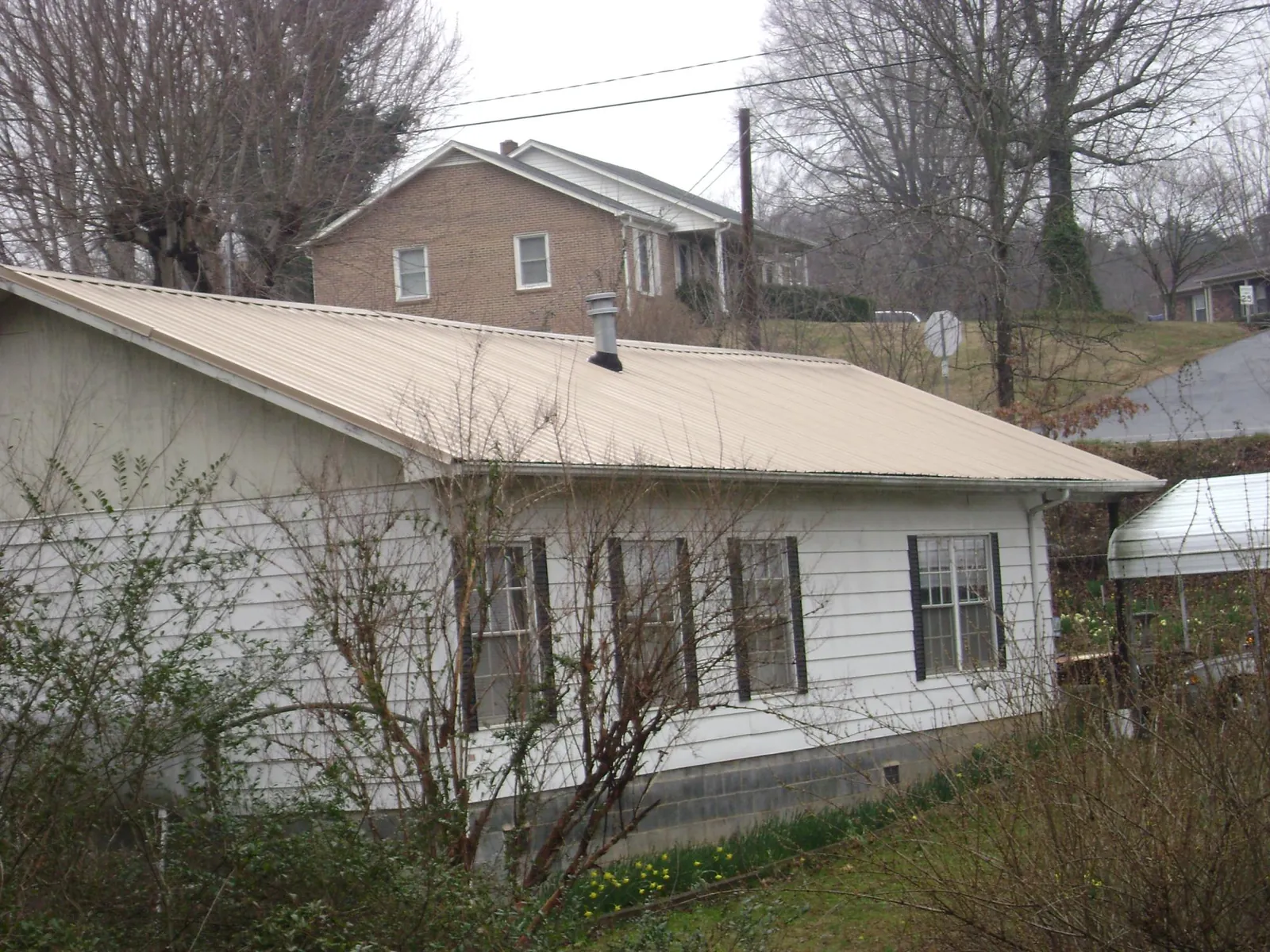 Tan metal roof on a white sided house set into a hillside — Commercial Roofing by Roofing Brothers in Hickman